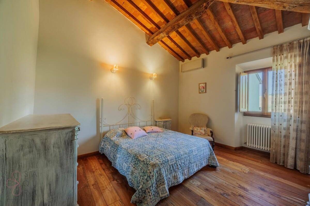 Schlafzimmer mit Holzboden, Holzbalkendecke und Fenster, das viel Tageslicht hereinlässt.
