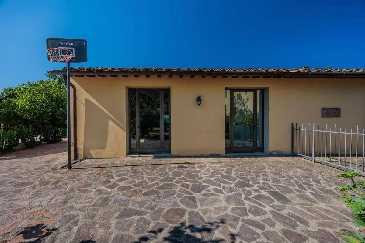 Außenansicht eines Nebengebäudes mit Basketballkorb und gepflastertem Vorplatz unter strahlend blauem Himmel.