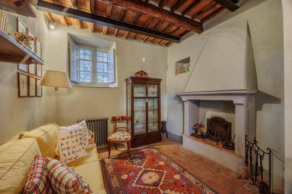Rustikales Wohnzimmer mit traditionellem Kamin, Terrakottaboden und sichtbaren Holzbalken an der Decke.