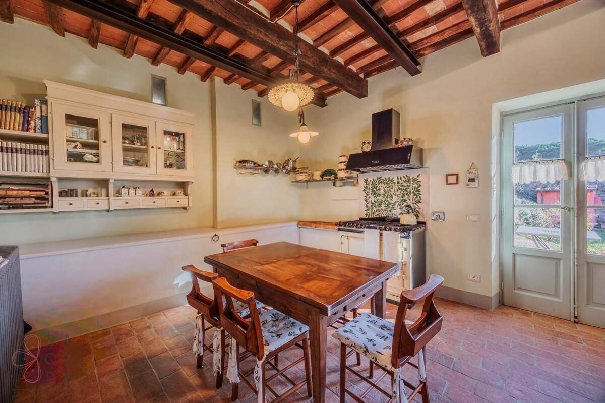 Traditionelle Küche mit Holztisch, Einbauschränken und einem klassischen Herd unter sichtbaren Holzbalken.