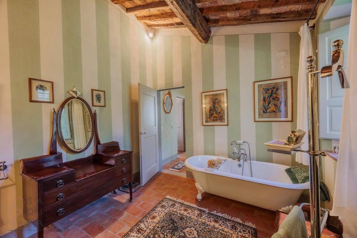Geräumiges Badezimmer mit freistehender Badewanne, gestreiften Wänden und Terrakottaboden.