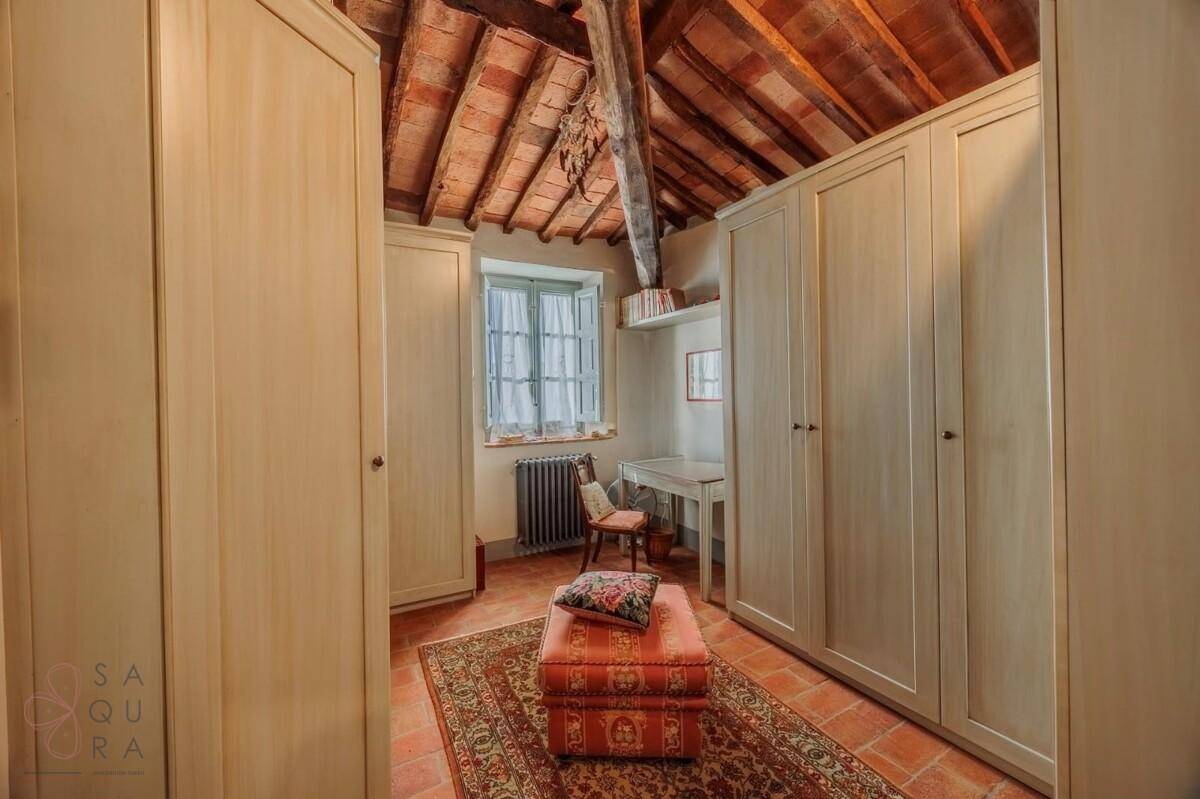 Zimmer mit Einbauschränken, Schreibtisch und Terrakottaboden unter einer Holzbalkendecke.
