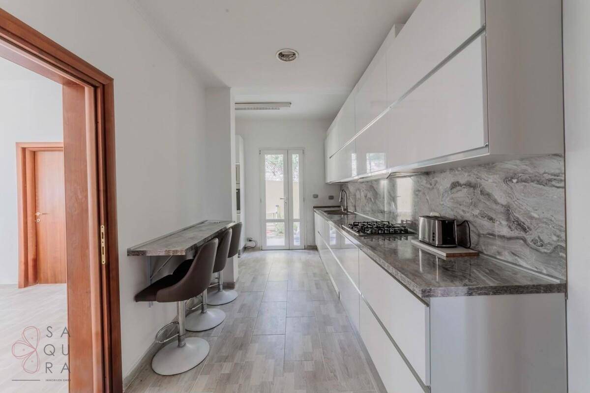 Moderne Küche mit weißen Hochglanzschränken, Granitarbeitsplatte und Frühstücksbar.