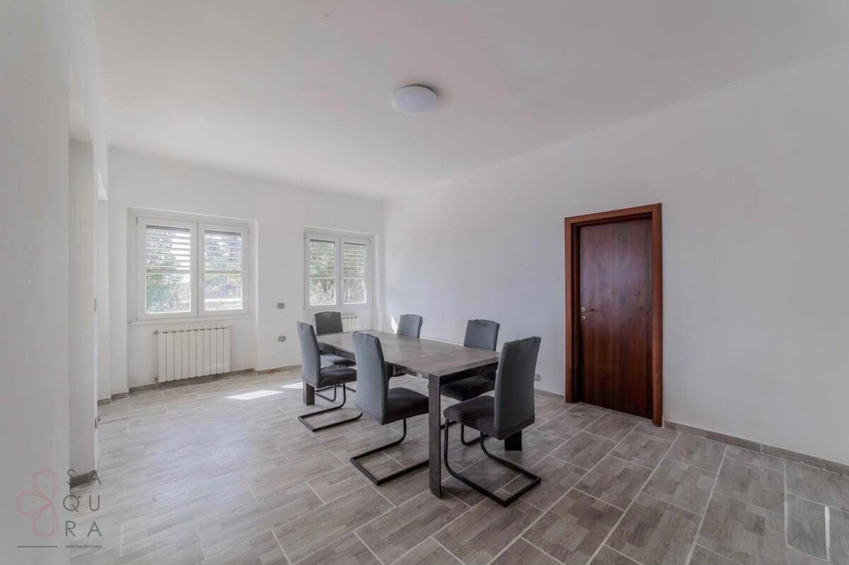 Heller Essbereich mit modernem Tisch und Stühlen, großen Fenstern und Fliesenboden.