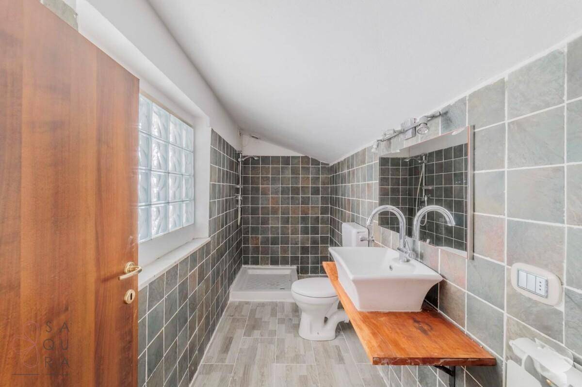 Badezimmer mit Dusche, Waschtisch, WC und Glasbaustein-Fenster, gefliest.