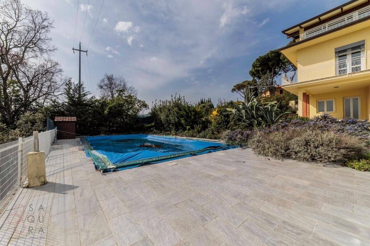 Außenbereich mit großem Pool, umgeben von hellen Fliesen und mediterraner Vegetation.
