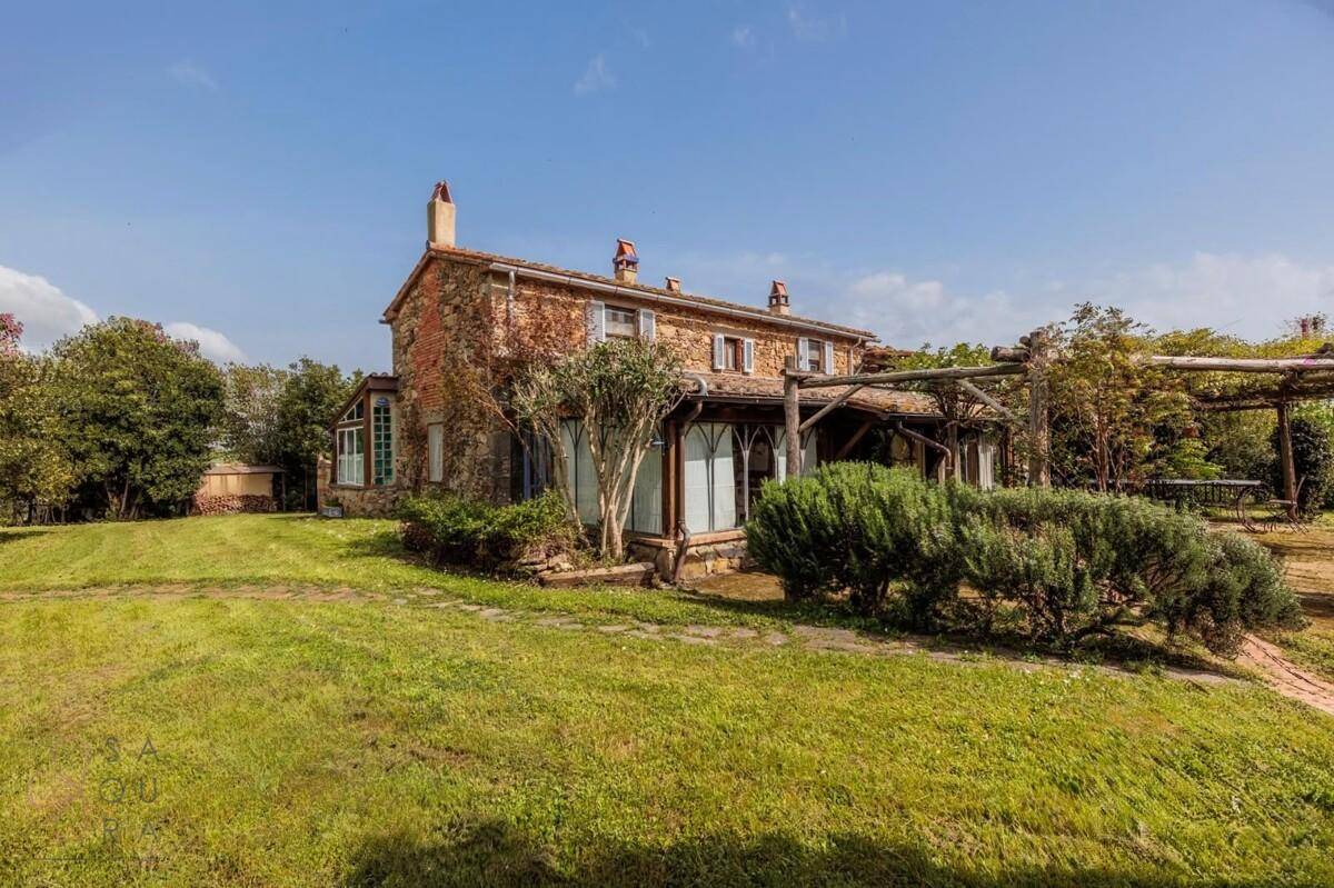 Charmantes Landhaus mit Steinfassade, umgeben von üppigem Grün und mediterraner Vegetation.