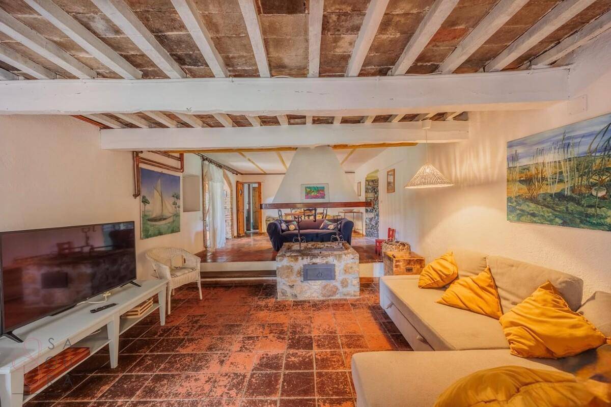 Rustikales Wohnzimmer mit sichtbaren Deckenbalken, Kamin und traditionellem Fliesenboden.