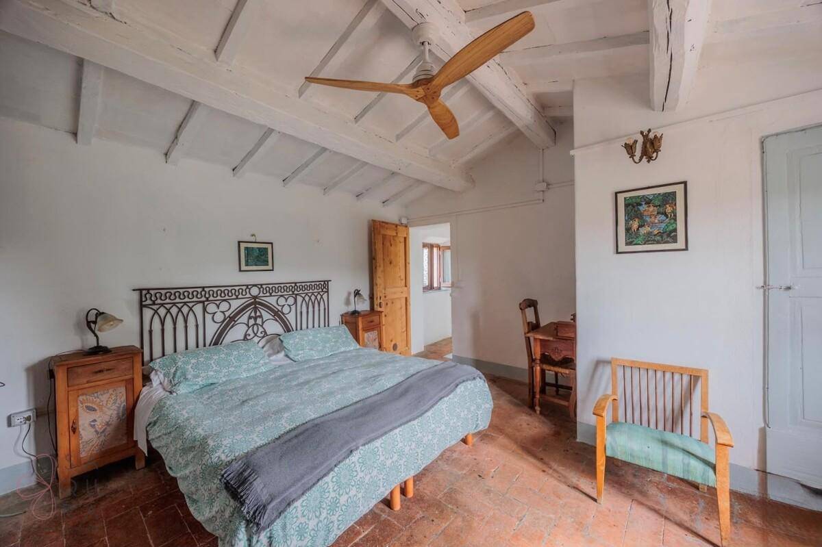 Helles Schlafzimmer mit Holzbalkendecke, Terrakottafliesen und einem großen Deckenventilator.