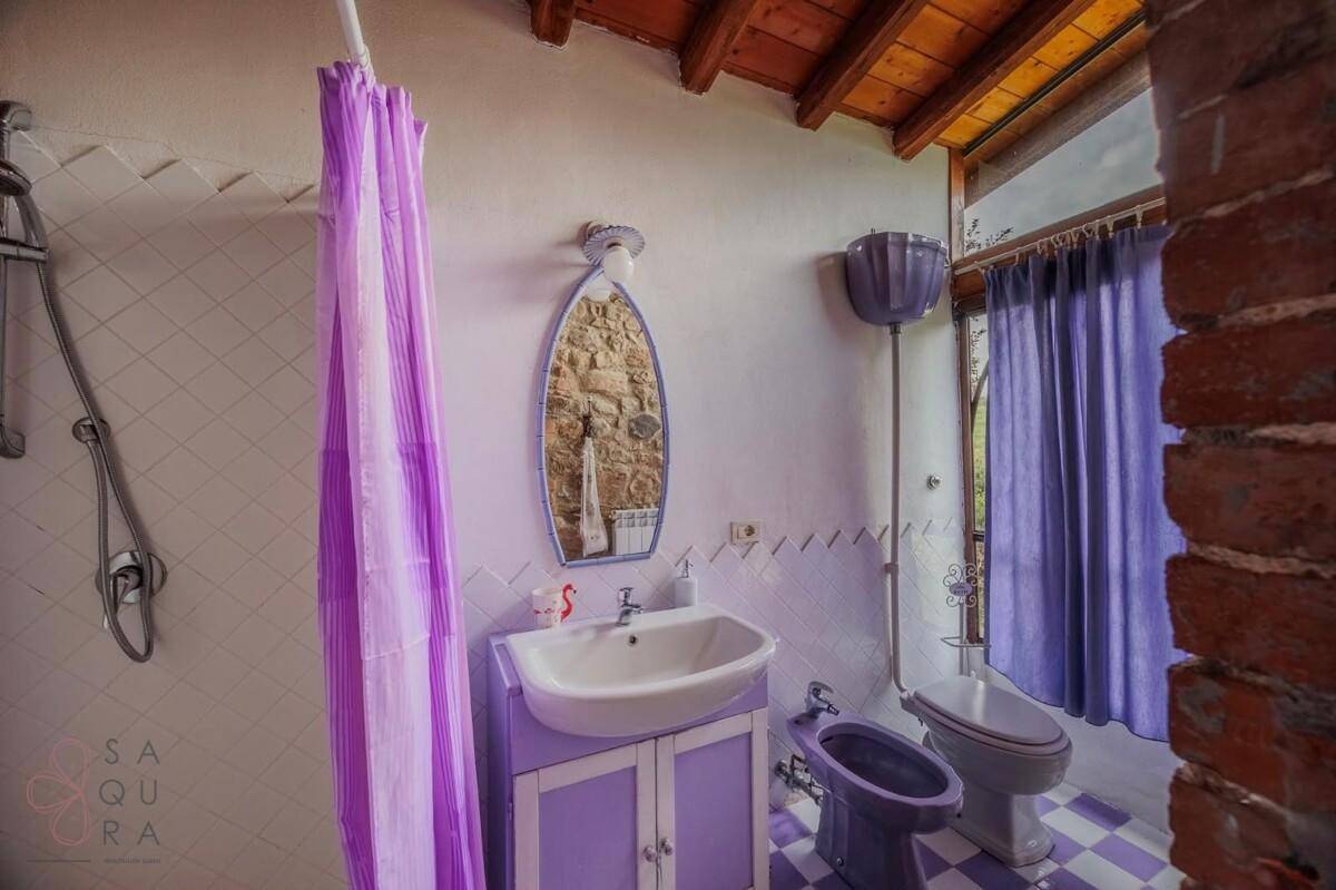 Badezimmer mit lila Akzenten, Waschbecken und Bidet, unter einer Holzbalkendecke.