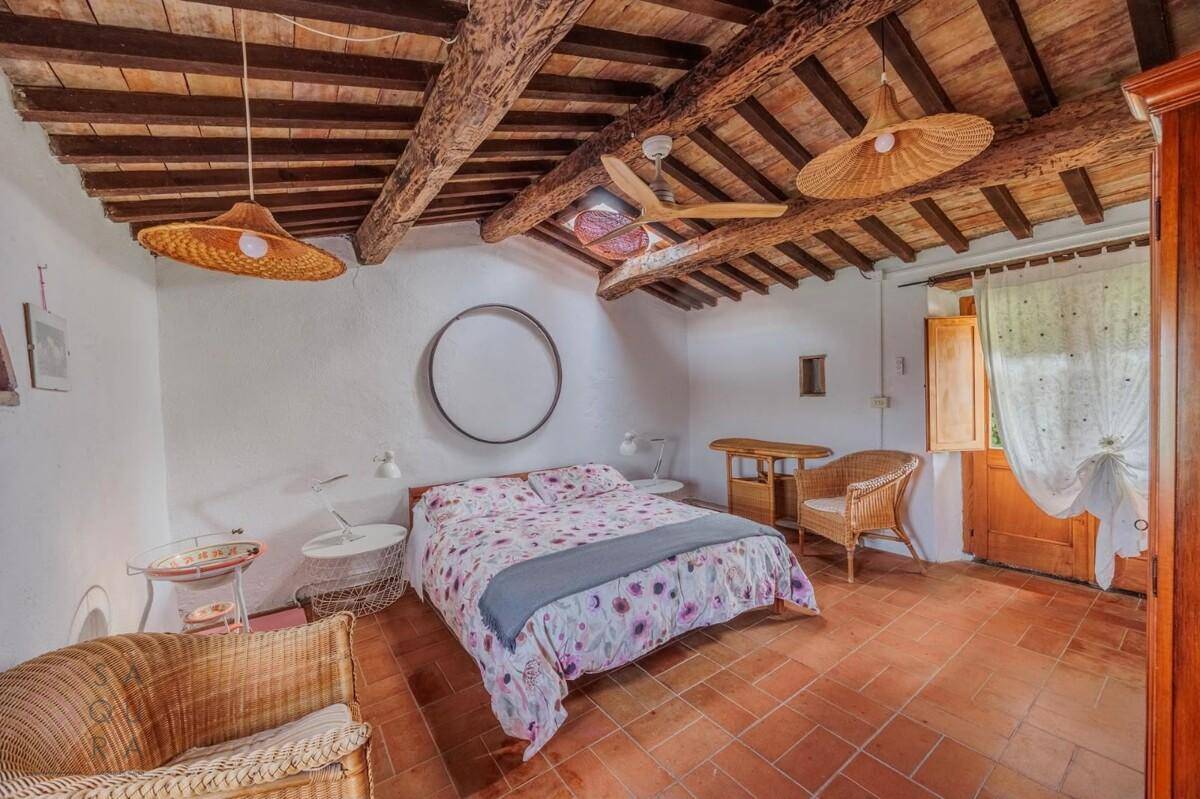 Gemütliches Schlafzimmer mit Holzbalkendecke, Terrakottafliesen und rustikalen Korbmöbeln.