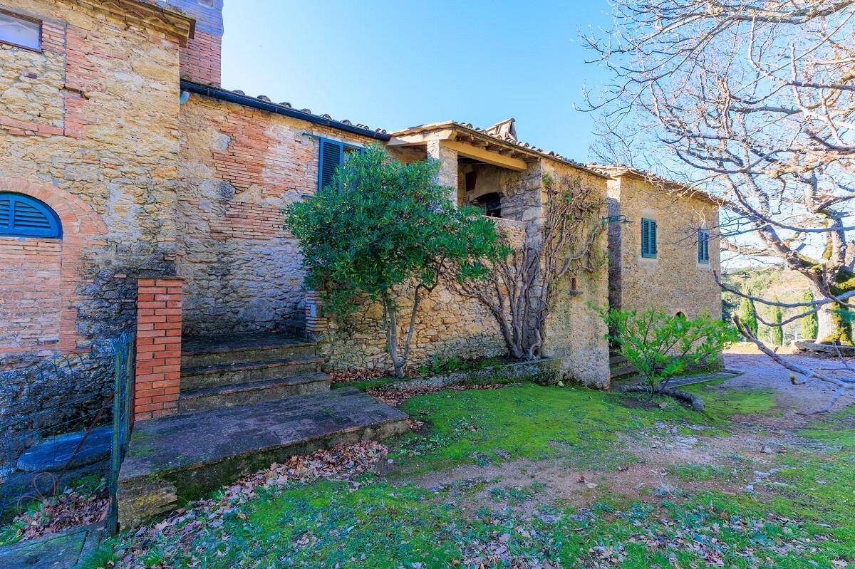 Rustikales Steinhaus mit Außentreppe und kleiner überdachter Loggia, umgeben von mediterraner Vegetation.