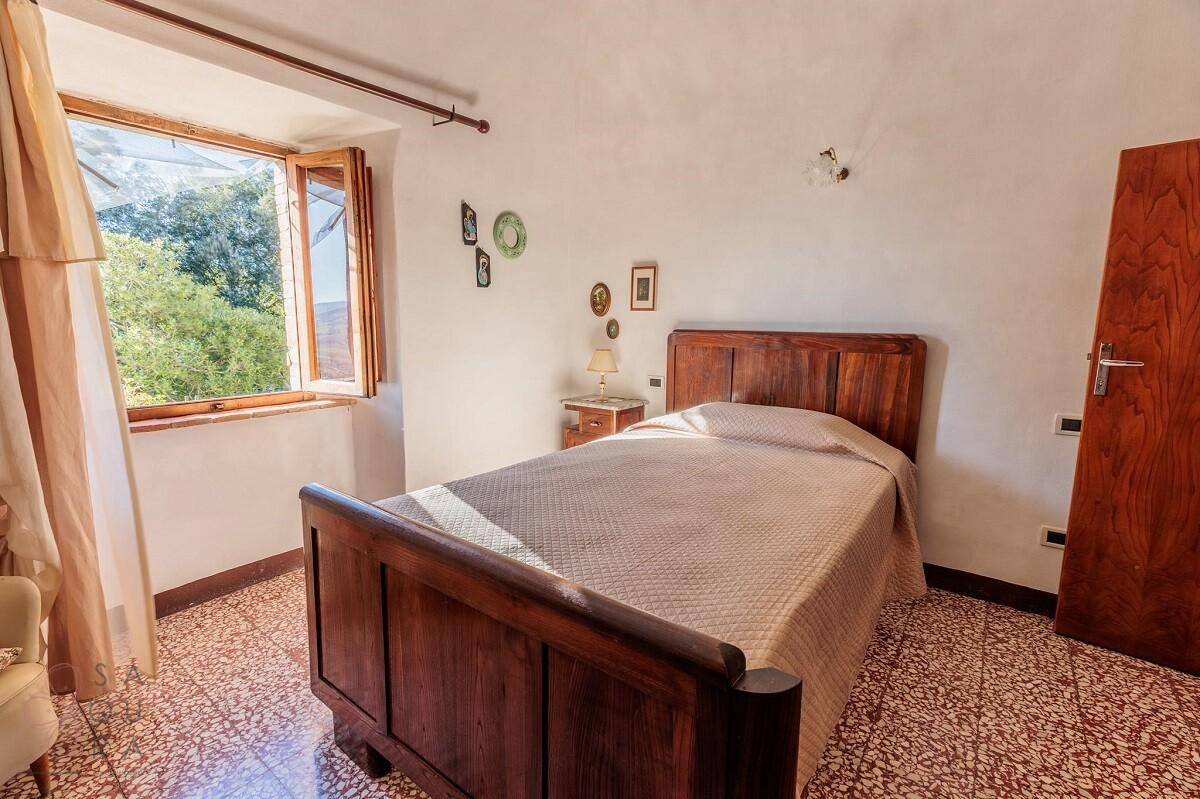 Helles Schlafzimmer mit Terrazzoboden, Holzbett und Fenster mit Blick auf die grüne Umgebung.