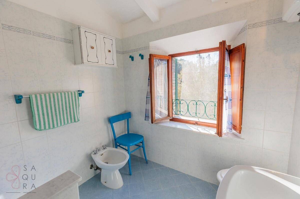 Helles Badezimmer mit hellblauen Fliesen, einem Bidet und einem Fenster mit Blick ins Grüne.