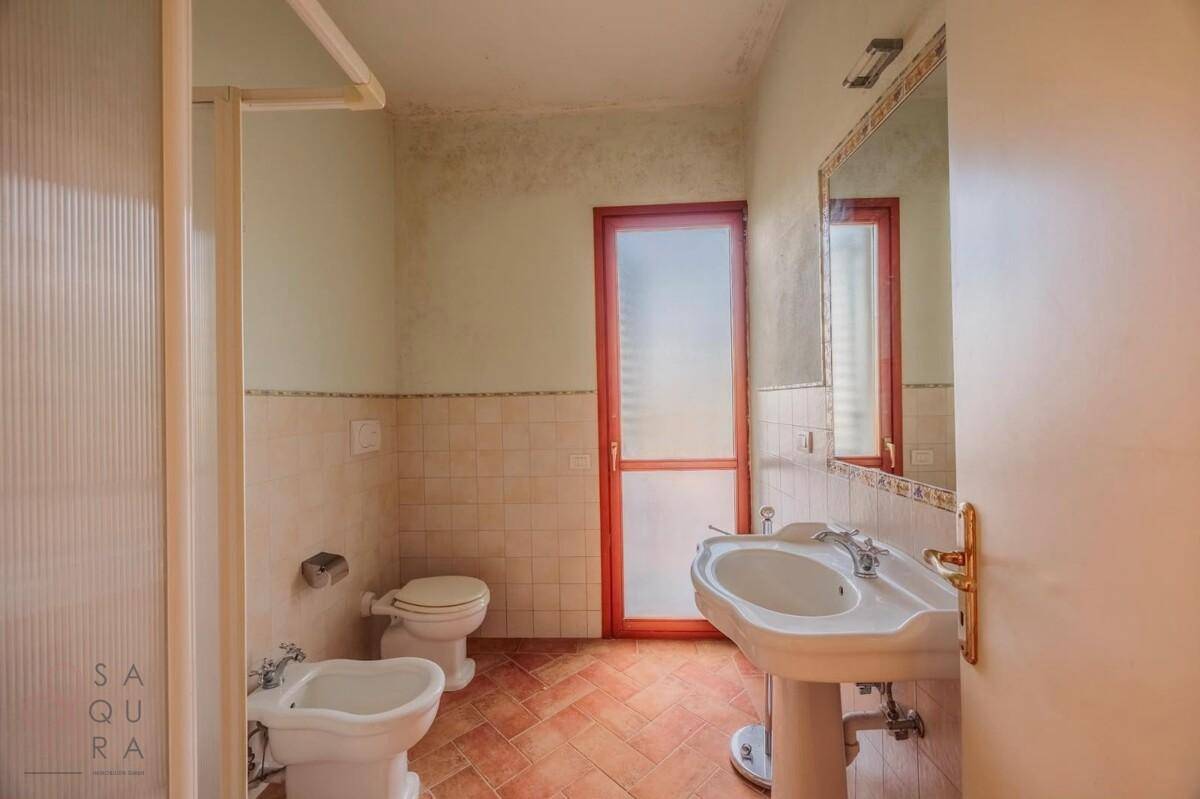 Badezimmer mit Waschbecken, WC, Bidet und Duschkabine, mit Terracotta-Fliesenboden.