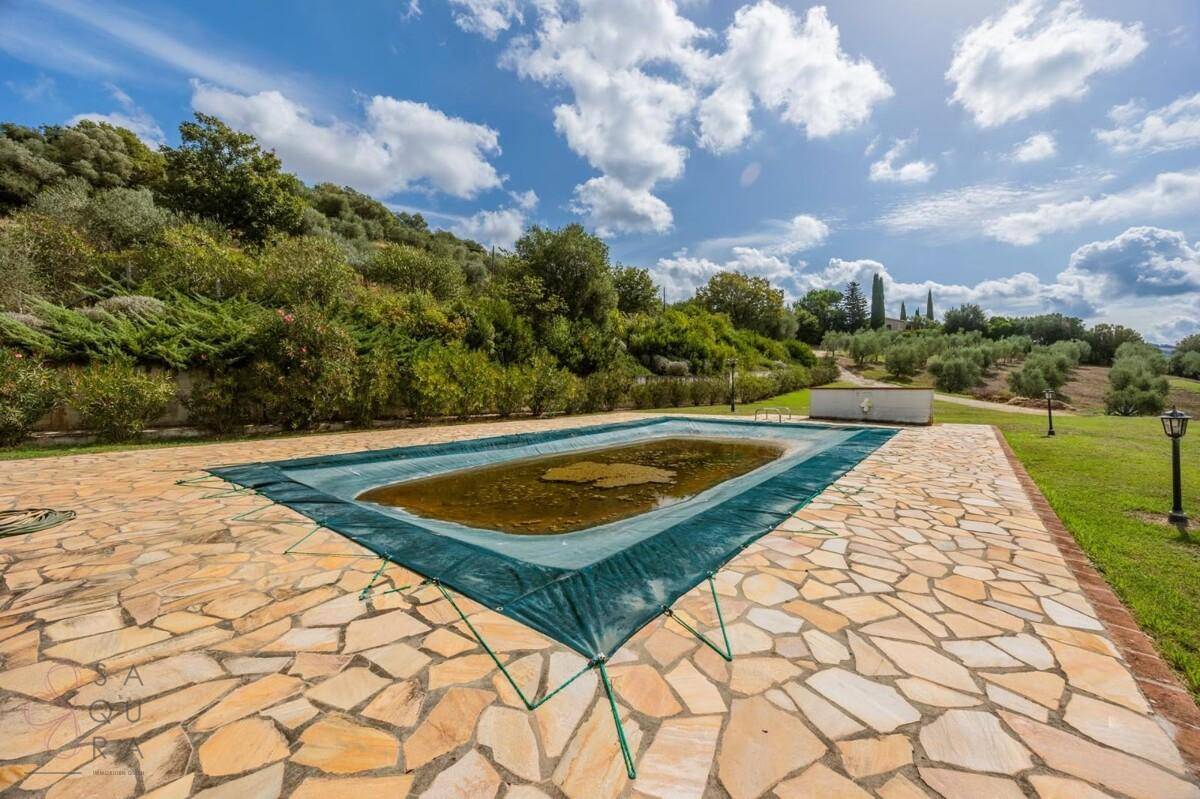 Der Poolbereich mit Steinplatten und einer Abdeckung, umgeben von mediterraner Vegetation.