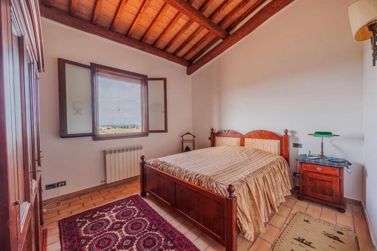 Helles Schlafzimmer mit Terrakottaboden, Holzbalkendecke und Fenster mit weitem Blick.