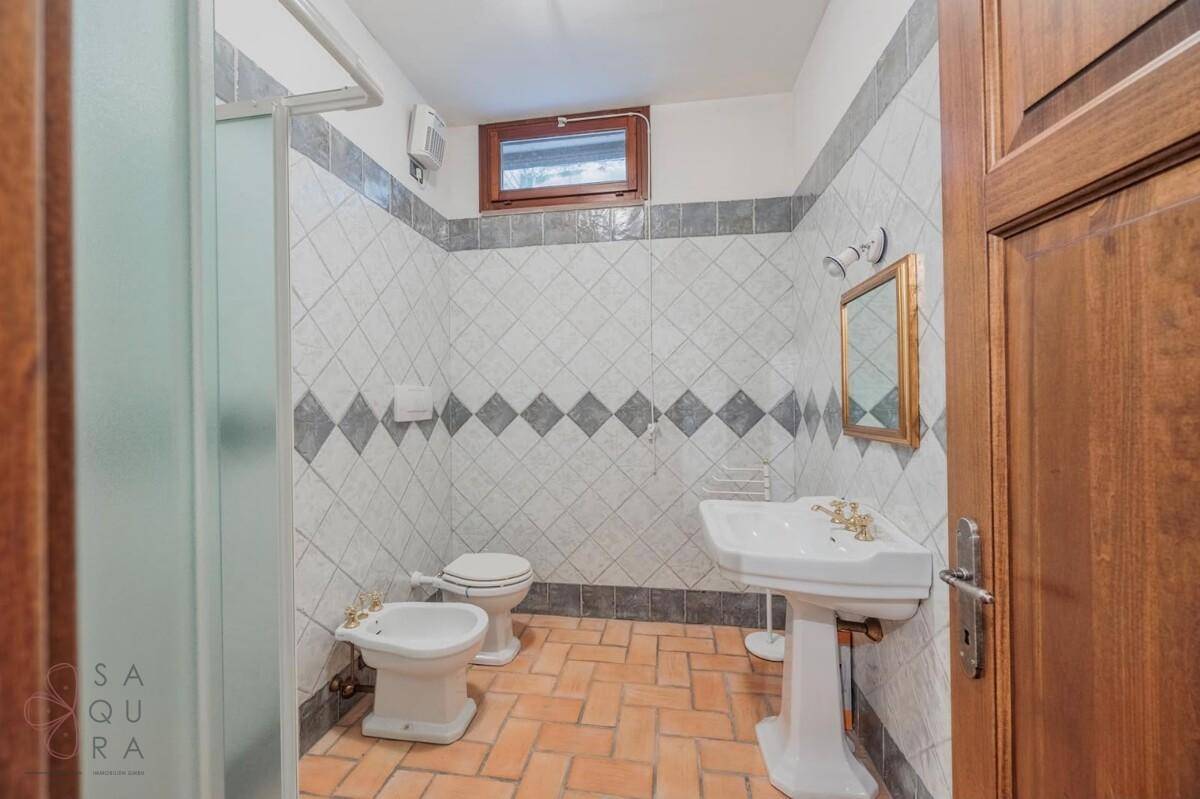 Badezimmer mit Duschkabine, WC, Bidet, Waschbecken und Terrakottaboden.