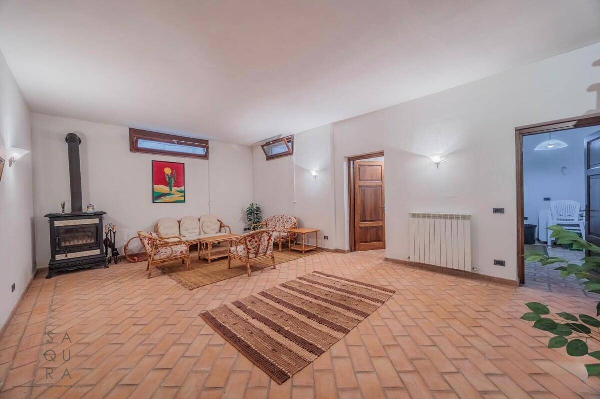 Geräumiger Wohnbereich im Untergeschoss mit Kaminofen, Korbmöbeln und Terrakottaboden.