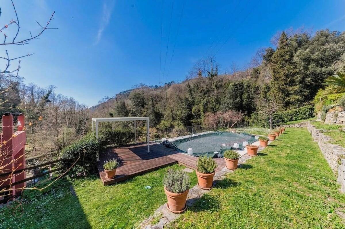 Gartenbereich mit Holzdeck, einem Pool und Topfpflanzen, umgeben von üppiger grüner Landschaft.