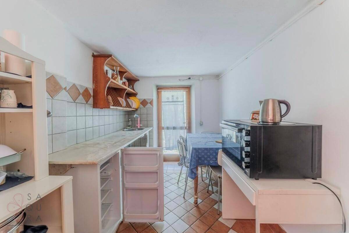 Kleine Küche mit einfachen Holzregalen, Kühlschrank und Mikrowelle, mit Zugang nach draußen.