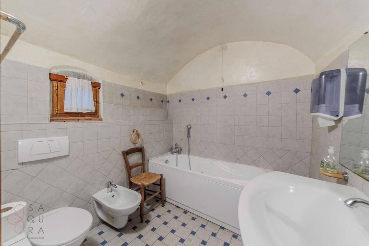 Badezimmer mit Badewanne, Bidet und WC, gefliest in hellgrau und blau, mit gewölbter Decke.