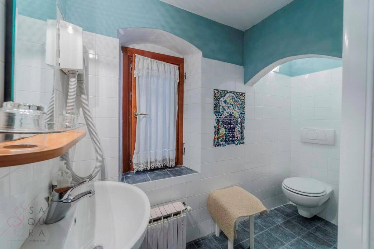 Badezimmer mit WC, Waschbecken und Fenster, gefliest in Weiß und Blau, mit traditionellen Akzenten.