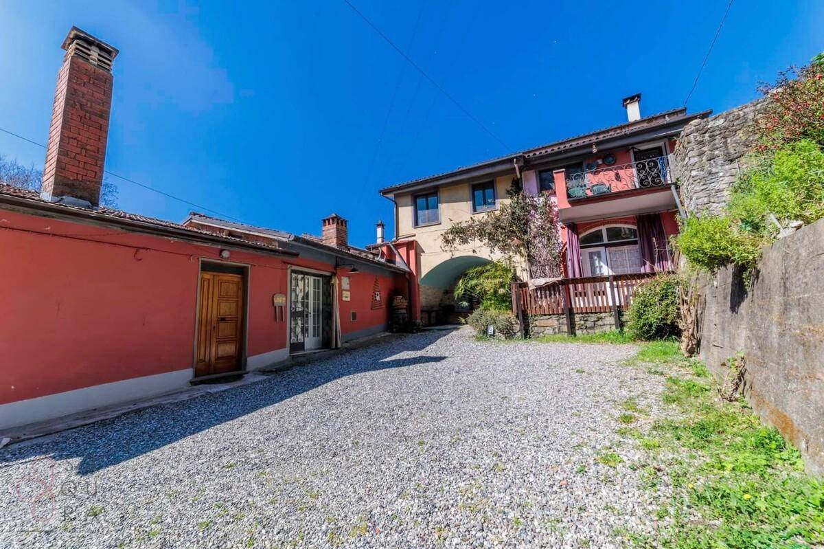 Kiesauffahrt zwischen zwei Gebäudeteilen mit einem Durchgang und traditioneller Architektur.