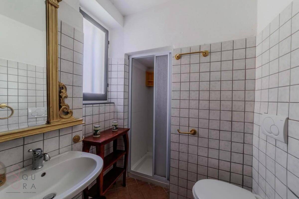 Badezimmer mit Duschkabine, Waschbecken und WC, gefliest in Weiß mit dunklen Fugen.