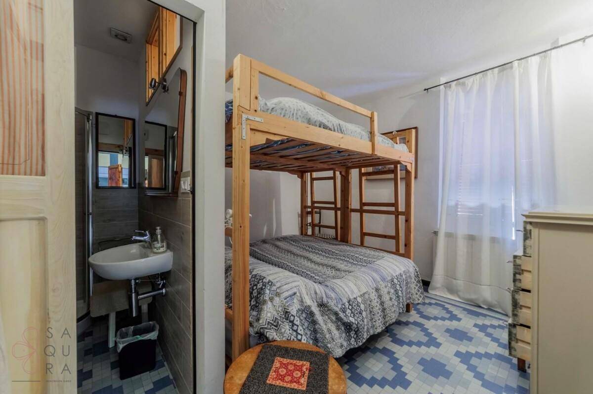 Schlafzimmer mit Etagenbett und einem kleinen Waschbeckenbereich, mit gemustertem Fliesenboden.