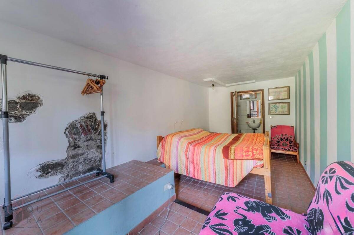 Schlafzimmer mit Einzelbett, gestreiften Wänden und einem Kleiderständer, mit Terrakottaboden.