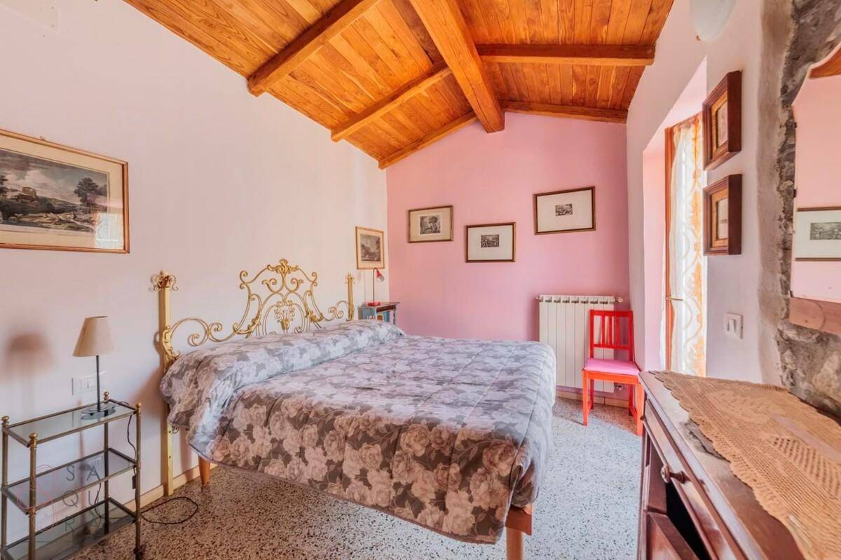 Schlafzimmer mit Doppelbett, rosafarbenen Wänden und einer Holzbalkendecke, mit Terrazzoboden.