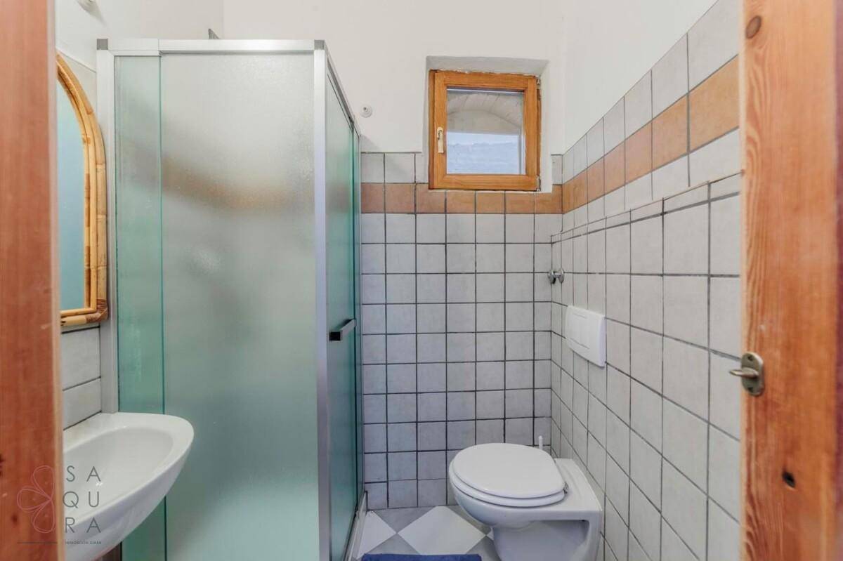 Badezimmer mit Duschkabine, Waschbecken und WC, gefliest in Weiß und Braun, mit Fenster.