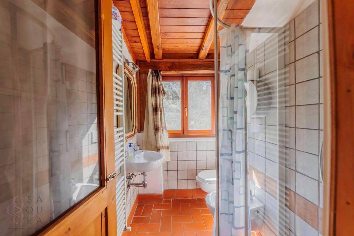 Badezimmer mit Dusche, WC, Waschbecken, Fenster und rustikalen Holzbalken an der Decke.