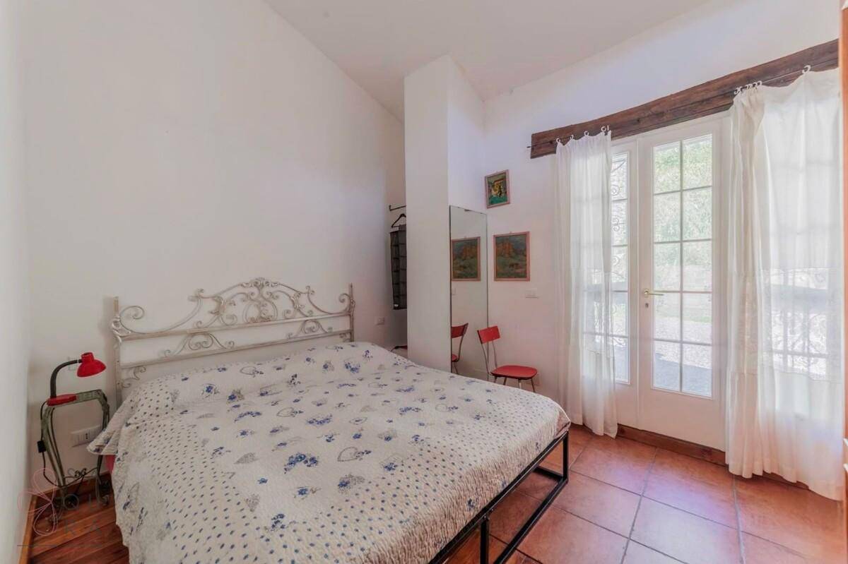 Schlafzimmer mit Doppelbett, weißen Wänden und großen Glastüren, die nach draußen führen.