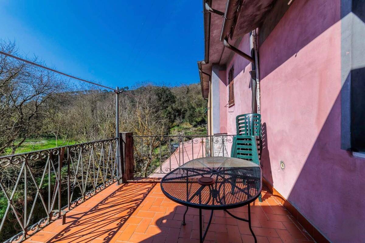 Balkon mit Metallmöbeln und Blick auf eine grüne, hügelige Landschaft unter blauem Himmel.