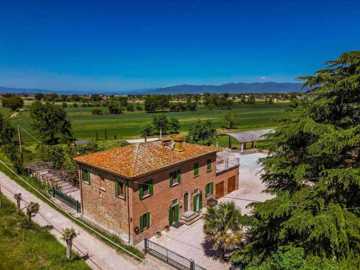 Panoramablick auf ein charmantes Landhaus mit Ziegeldach, umgeben von üppigen Feldern und Bäumen.