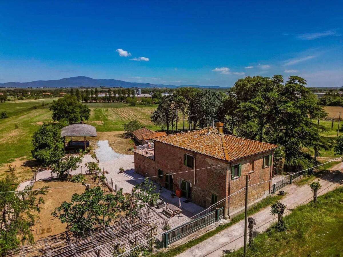 Weitläufige Luftaufnahme eines Landhauses umgeben von grünen Feldern und Bergen im Hintergrund.