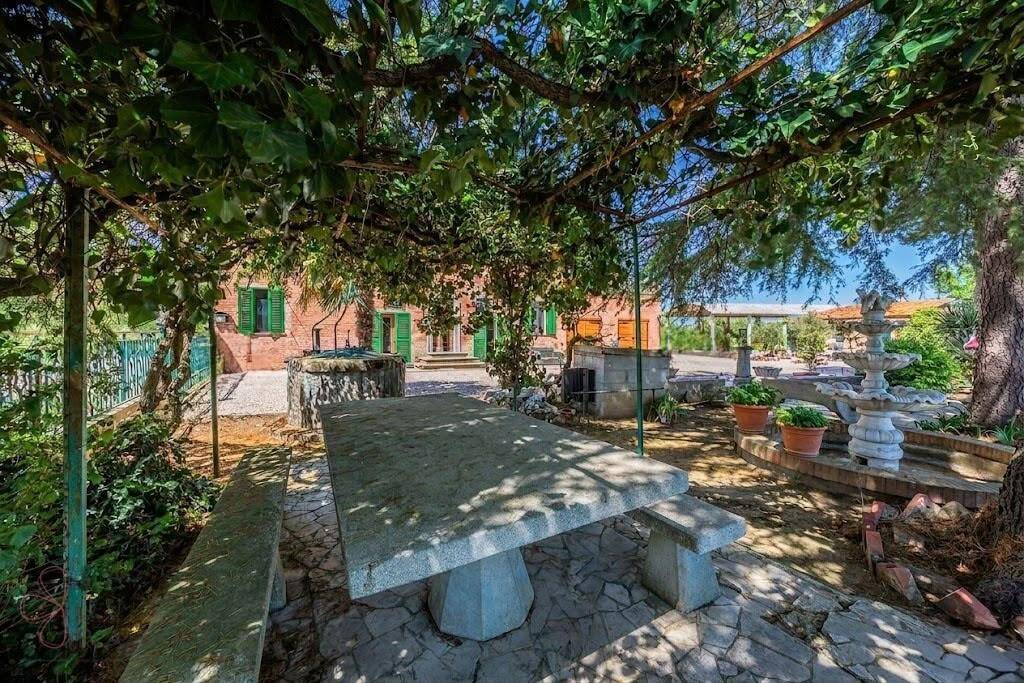 Gemütlicher Essbereich im Freien unter einer bewachsenen Pergola mit Steintisch und Brunnen.