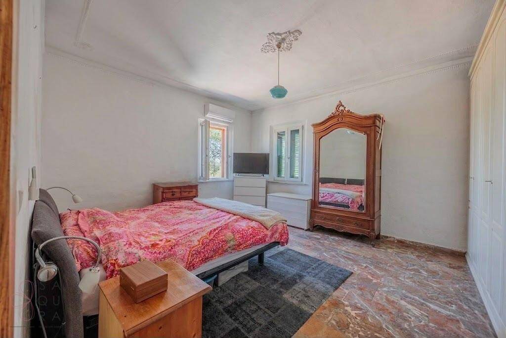 Schlafzimmer mit Terrazzoboden, traditionellem Holzschrank und Fenster mit Blick ins Grüne.