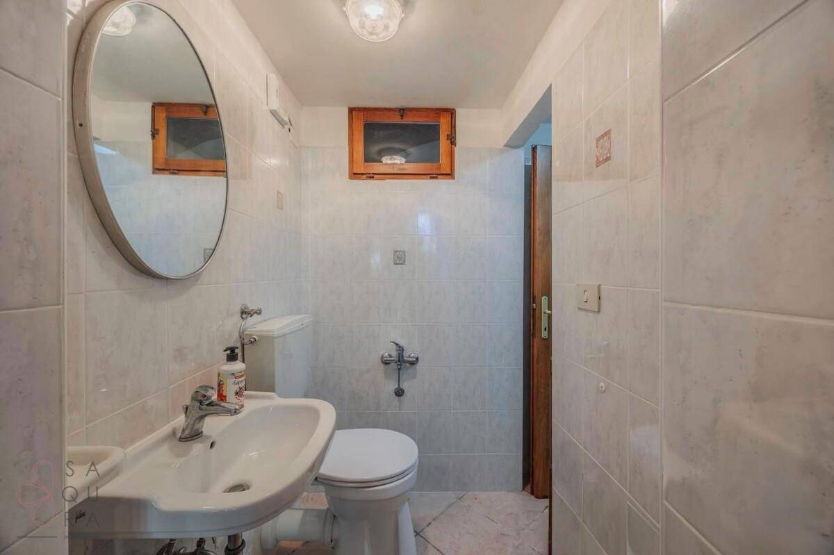 Kleines Badezimmer mit weißen Fliesen, Waschbecken und Toilette.