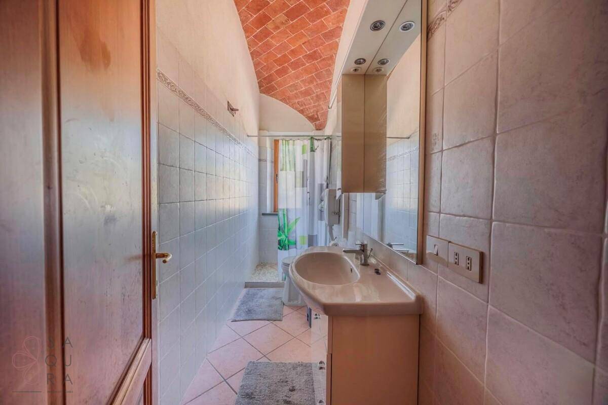 Schlichtes Badezimmer mit Dusche, Waschbecken und Gewölbedecke aus Ziegeln.