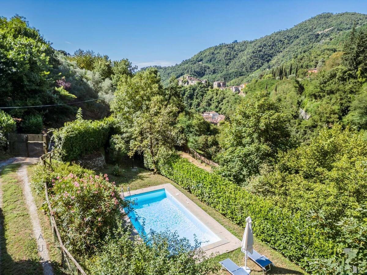 Erfrischender Poolbereich mit Liegestühlen und Sonnenschirm, umgeben von üppiger Natur und Hügeln.