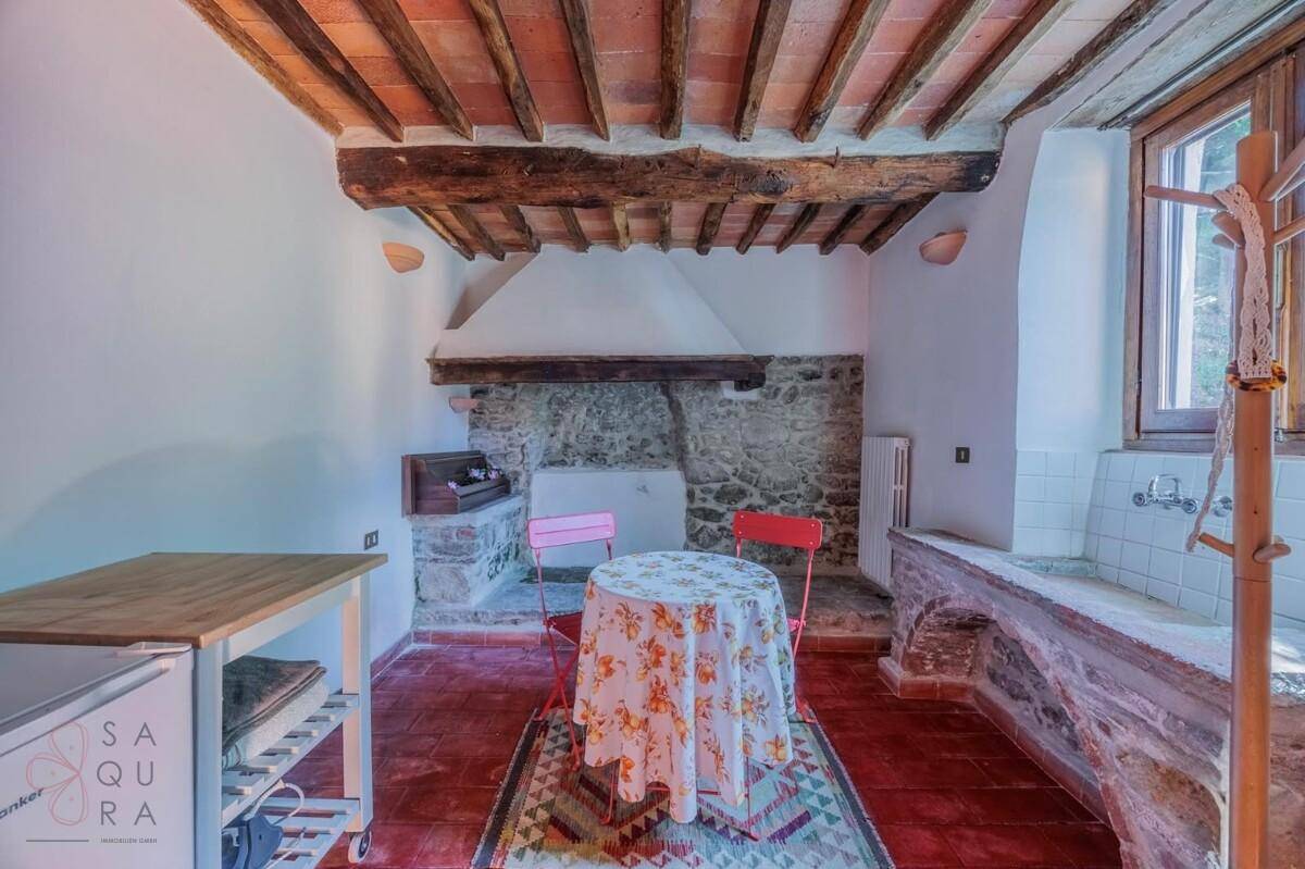 Rustikale Küche mit offenem Kamin, Holzbalkendecke und Terrakottaboden, ideal für traditionelles Kochen.