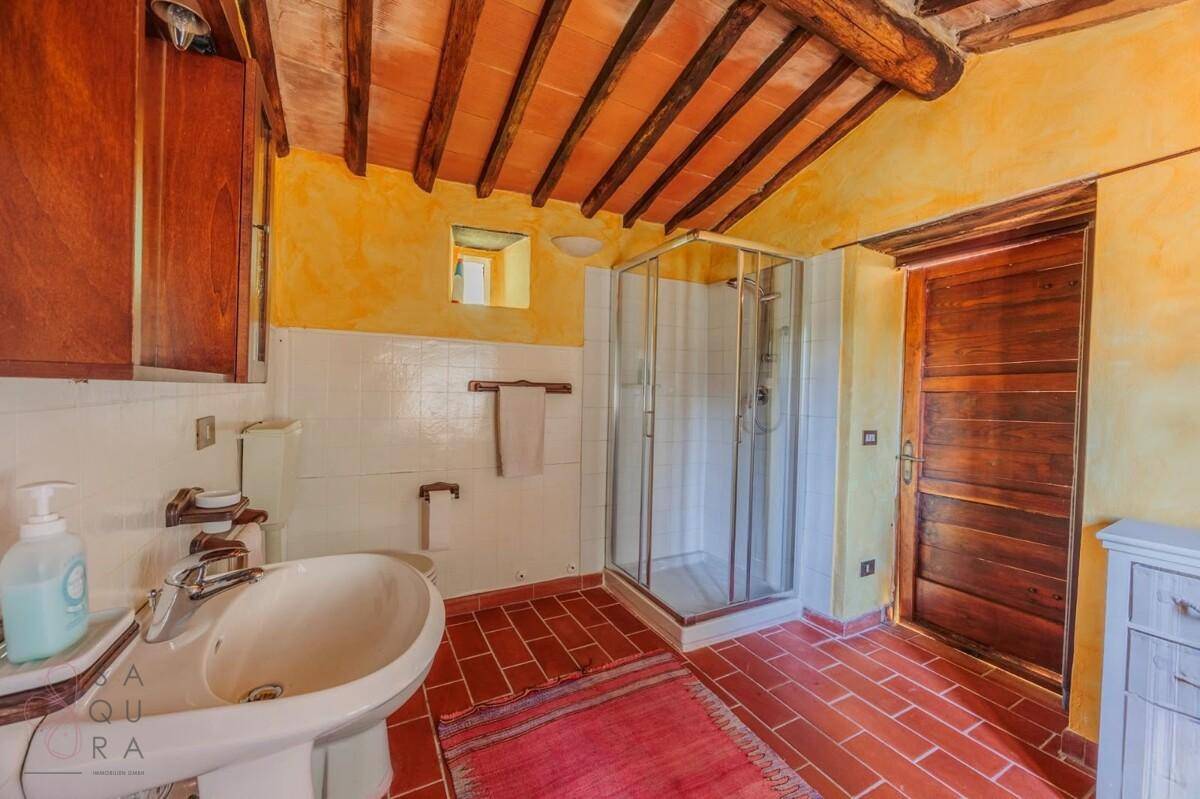 Rustikales Badezimmer mit Terrakottaboden, Holzbalkendecke und einer Duschkabine.