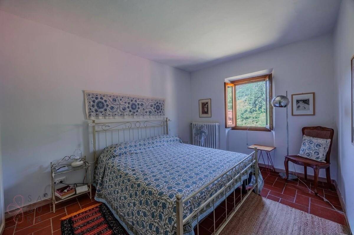 Helles Schlafzimmer mit Terrakottaboden, schmiedeeisernem Bett und Blick ins Grüne.