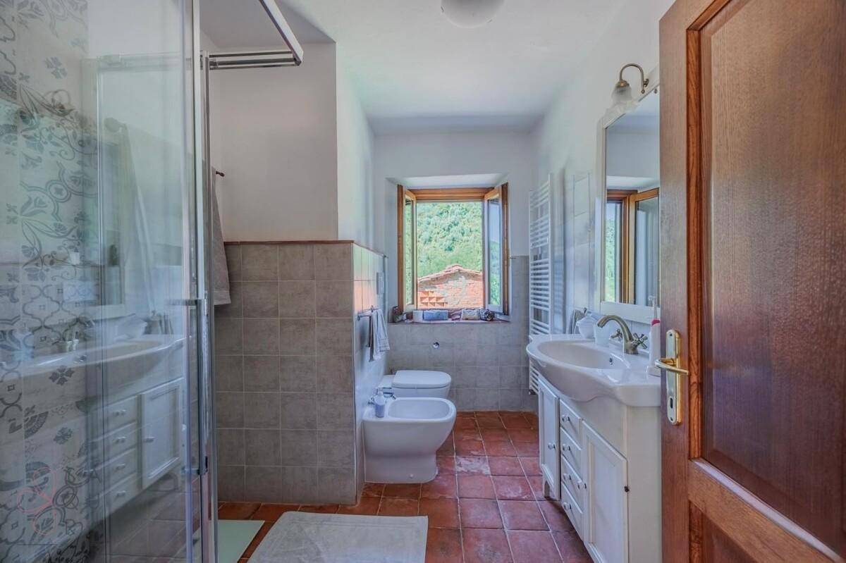 Helles Badezimmer mit Terrakottaboden, Dusche, Bidet und Fenster mit Blick ins Grüne.