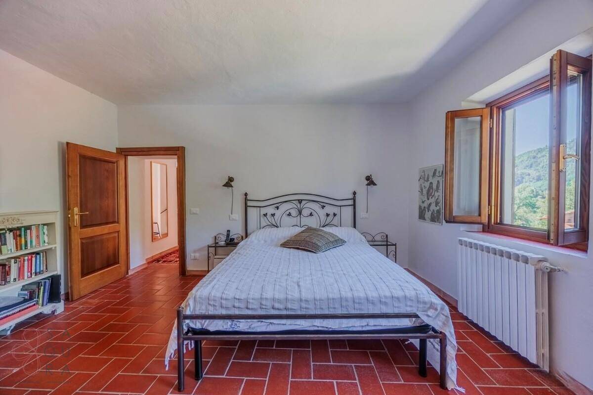 Geräumiges Schlafzimmer mit Terrakottaboden, Doppelbett und zwei Fenstern für viel Licht.