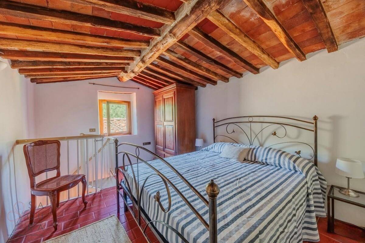 Gemütliches Schlafzimmer mit Terrakottaboden, Holzbalkendecke und schmiedeeisernem Bett.