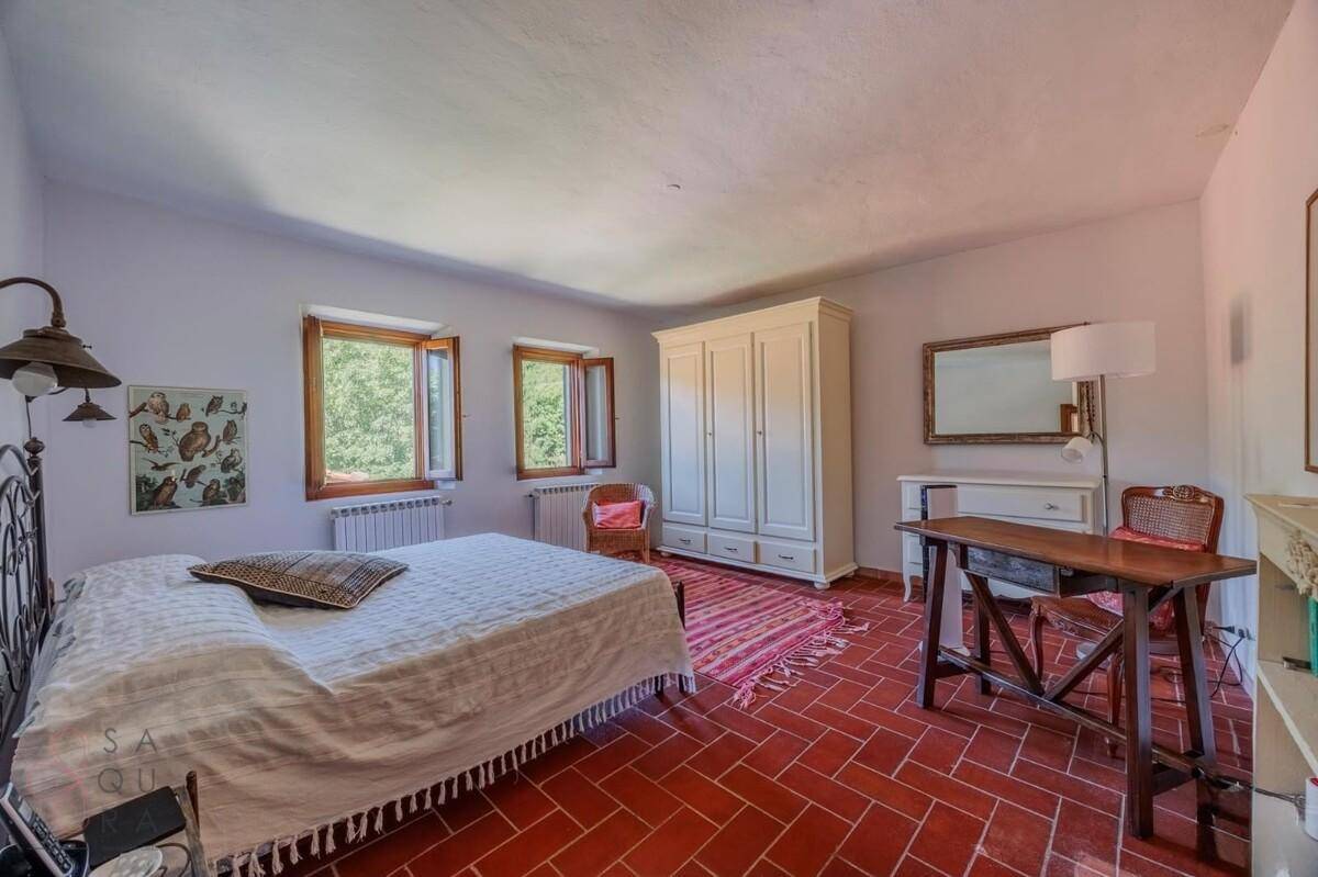 Großes Schlafzimmer mit Terrakottaboden, weißem Kleiderschrank und Schreibtisch am Fenster.